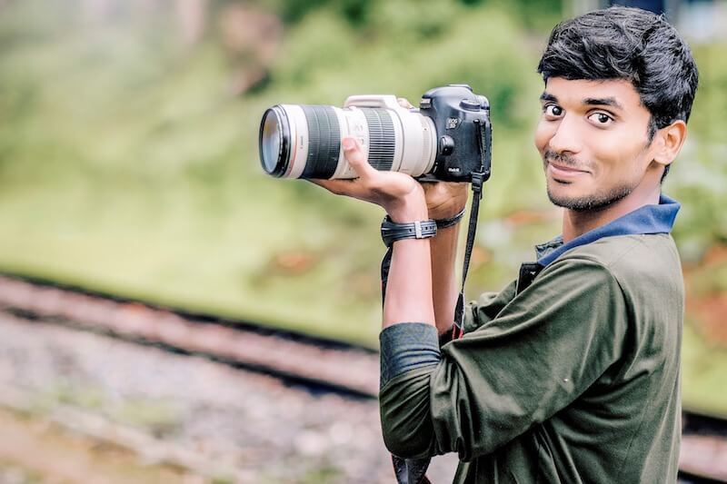 An Indian man holding a camera with a telephoto lens